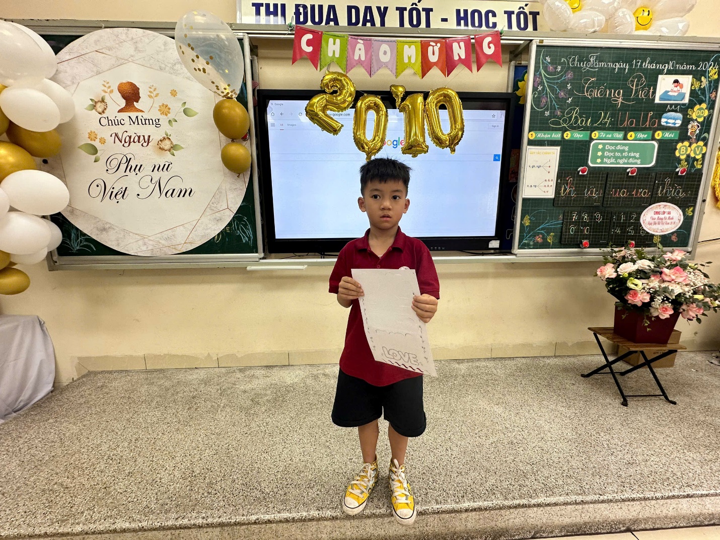 A child holding a piece of paper in front of a classroomDescription automatically generated