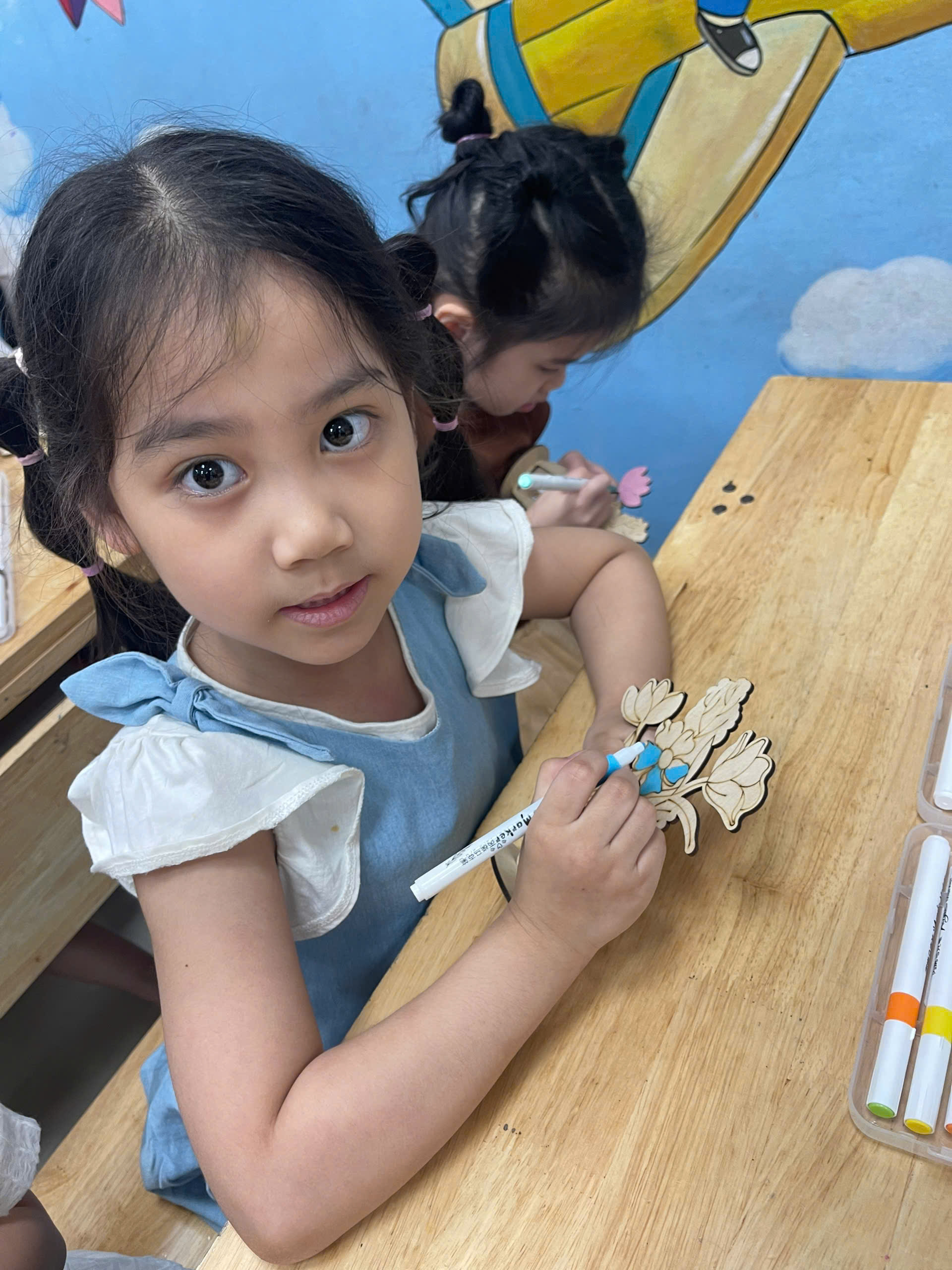 A child sitting at a table with a pen and a butterflyDescription automatically generated