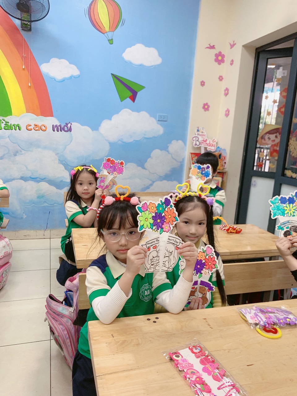 A group of children sitting at desks holding up paper flowersAI-generated content may be incorrect.