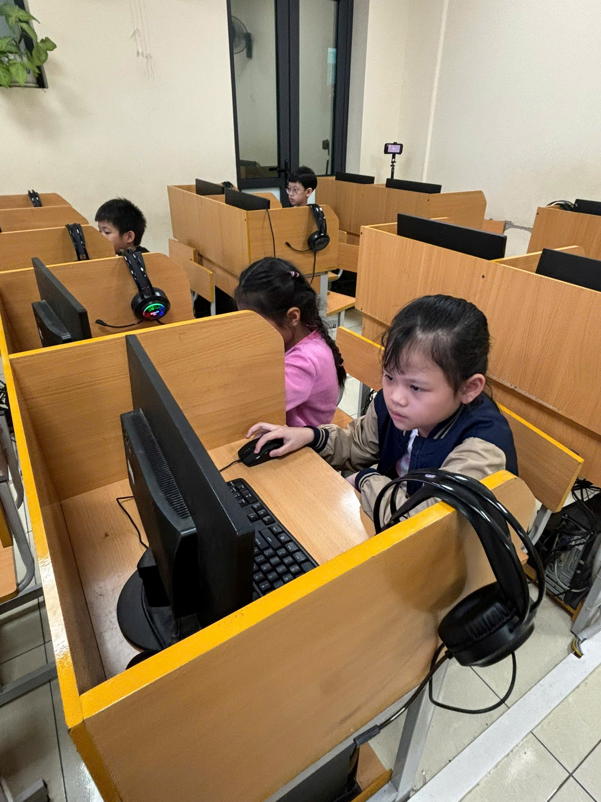 A group of children sitting at desks in a room with computersAI-generated content may be incorrect.